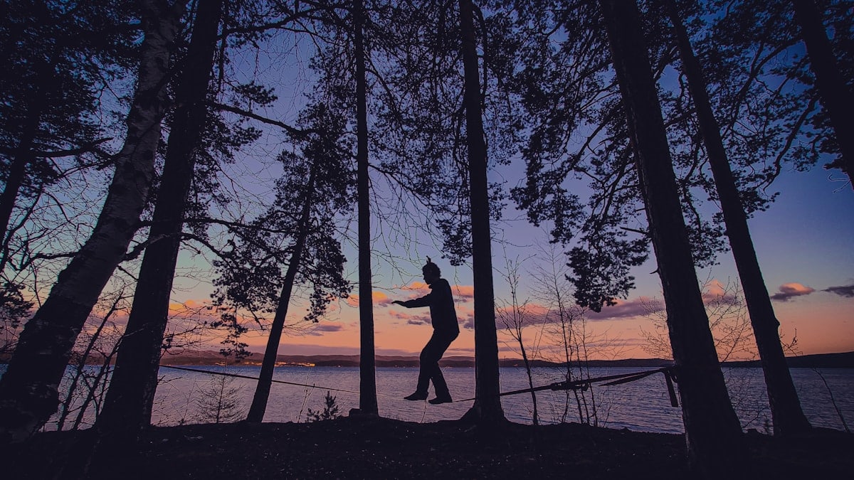 Person balancing on a slackline between trees at sunset.